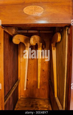 Drei rustikale Holzschuhtragen hängen in einem alten Holzschrank mit einem kunstvoll geschnitzten Design auf der oberen Platte. Die Elemente sind beleuchtet Stockfoto