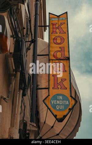 Ein verwittertes, aufrechtes Vintage-Kodak-Schild mit „PRODOTTI“ oben und einem Pfeil nach unten mit „IN VENDITA QUI“ (HIER ZUM VERKAUF) am unteren Rand Stockfoto