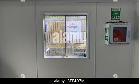 Eine Defibrillatorbox an einer Wand neben einem Fenster mit einem Schild von Taylor Wimpey bei Taylor Wimpey Woodside Vale, Leeds, Großbritannien. Stockfoto