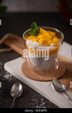 Schichten cremiger Chiasamenpudding und lebendiges Mangopüree werden mit frischen Mangobacken und Kokosnuss garniert. Weiche natürliche Seitenbeleuchtung Stockfoto