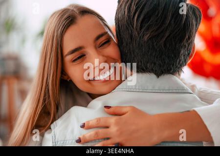 Glückliche junge Frau, die zu Hause einen Freund umarmt, lächelnder romantischer Partner, der einen liebevollen Moment in einem gemütlichen, modernen Wohnzimmer genießt Stockfoto
