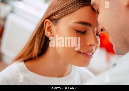 Romantisches junges Paar, das zu Hause intime Momente teilt, Mann küsst Frau auf die Stirn in sanftem Nahporträt Stockfoto