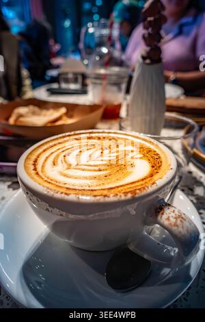 Nahaufnahme eines Cappuccino-Kaffees auf einem Tisch, während Sie sich mit Freunden in einem Café unterhalten Stockfoto