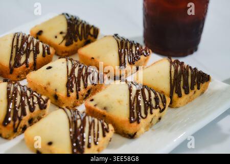 Viele quadratische Muffins mit Schokoladensoße auf weißem Teller serviert mit Eiskaffee Stockfoto