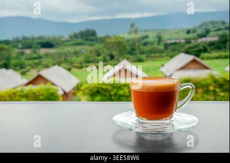 Heißer Thai-Milchtee in einer Tasse mit Blick auf die Berge, wenn es von weit her regnet Stockfoto