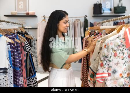 Junge Indianerin, die im Modegeschäft Kleidung sucht Stockfoto
