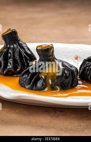 Schwarze hinkali-Knödel mit Sauce auf Teller Stockfoto