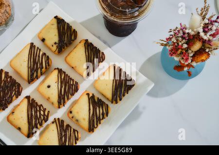 Viele quadratische Muffins mit Schokoladensoße auf weißem Teller serviert mit Eiskaffee. Stockfoto