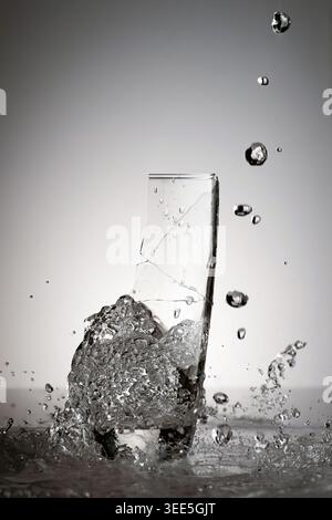 Ein Glas bricht durch das Gießen von Trinkwasser mit vielen spritzenden Tropfen auf. Stockfoto