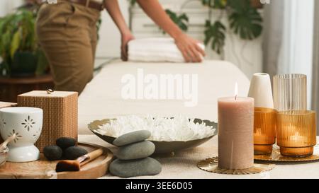 Entspannender Spa-Behandlungsraum mit Massagetisch, beleuchteter Kerze, heißen Steinen und gefaltetem Handtuch Stockfoto