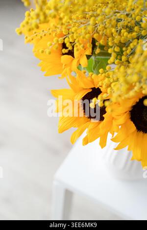 Blüte von Mimosa-Blumen und Sonnenblumen in weißer Keramikvase auf weißem Backsteinmauerhintergrund mit Platz für Text. Frühlingskonzept, gelbe Farbe Stockfoto