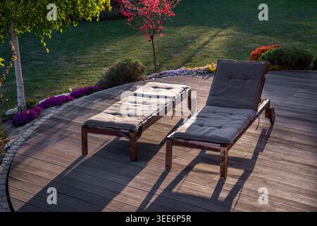 Garten-Entspannungsbereich, zwei hölzerne Sonnenliegen auf einer Terrasse in einem wunderschönen Garten Stockfoto