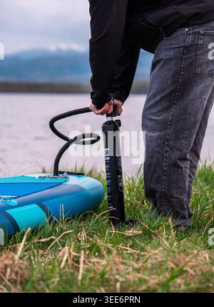 Mann, der blaues aufblasbares Stehpaddelbrett mit Handpumpe aufbläst Stockfoto