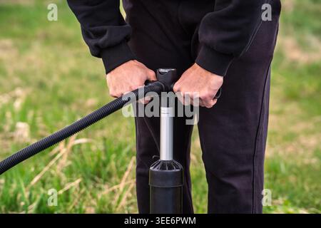 Mittelteil einer Person, die Ausrüstung mit einer Handpumpe im Freien aufpumpt Stockfoto