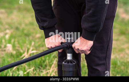 Mittelteil einer Person, die Ausrüstung mit einer Handpumpe im Freien aufpumpt Stockfoto
