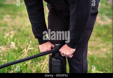 Mittelteil einer Person, die Ausrüstung mit einer Handpumpe im Freien aufpumpt Stockfoto