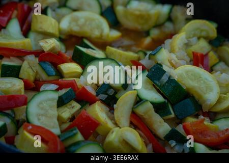 Blick auf geschnittene grüne und gelbe Zucchini gemischt mit roten Paprika und Zwiebeln, die in einer Pfanne in Moab, Utah, USA, kochen. Stockfoto