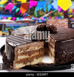 Köstlicher Schokoladenkuchen mit Brigadeiro-Toppings und Streuseln, vor einem lebhaften, verschwommenen Festa Junina Hintergrund mit bunten Fahnen. Stockfoto