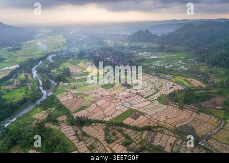 Aus der Vogelperspektive auf die üppigen Reisterrassen von Sidemen und einen sich windenden Fluss, der unter einem bewölkten Himmel durch das tropische Tal fließt, in Sidemen, Bali, Indonesien. Stockfoto
