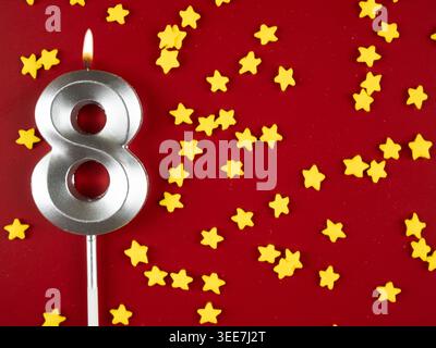 Konzept der Geburtstagsfeier und Jubiläumsfeier. Nummer 8: Silberne Geburtstagskerze auf festlichem rotem Hintergrund. Acht Jahre Geburtstag. Fl Stockfoto