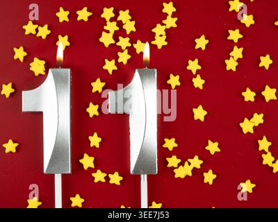 Konzept der Geburtstagsfeier und Jubiläumsfeier. Nummer 11 11 silberne Geburtstagskerze auf festlichem rotem Hintergrund. Elf Jahre Geburtstag. Stockfoto