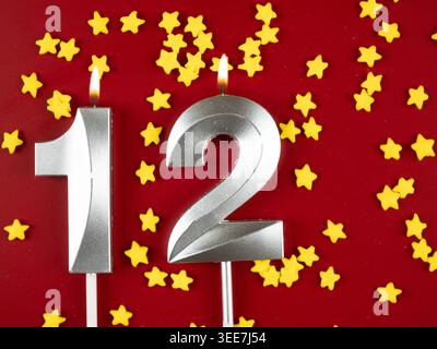 Konzept der Geburtstagsfeier und Jubiläumsfeier. 12. Silberne Geburtstagskerze auf festlichem rotem Hintergrund. Zwölf Jahre Geburtstag. Stockfoto