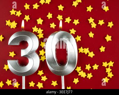 Konzept der Geburtstagsfeier und Jubiläumsfeier. Nummer 30 dreißig silberne Geburtstagskerze auf festlichem rotem Hintergrund. 30 Jahre Geburtstag. Stockfoto