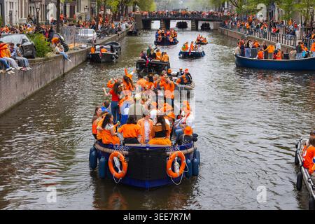 Amsterdam, Niederlande - 27. April 2026: Die Menschenmassen genießen den Königstag auf den Kanälen von Amsterdam, während sie orange tragen und mit Booten und feiern Stockfoto