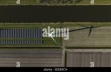 Luftaufnahme einer Windkraftanlage, die einen langen Schatten über Solarpaneele und landwirtschaftliche Felder neben einem Kanal wirft Niederlande. Stockfoto