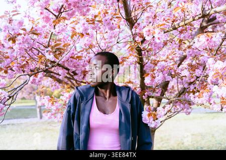 Durchdachter schwarzer Läufer, der nach dem Workout unter blühenden Sakura-Bäumen ruht Stockfoto