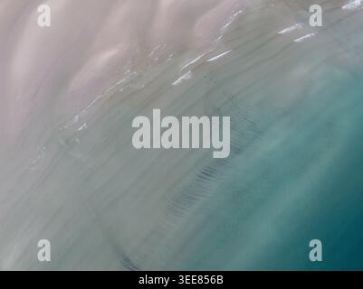 Blick aus der Vogelperspektive auf Gruinard Bay mit sanften türkisfarbenen Wellen, die über die Sandküste ziehen, und gewellten Texturen unter dem klaren Wasser in Gruinard, Schottland, Stockfoto