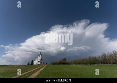 Eine einsame, weiße Kirche mit einem Turm steht vor einem dramatischen Himmel, der mit hohen Sturmwolken und einer klaren blauen Weite gefüllt ist, die ein Gefühl von IS weckt Stockfoto