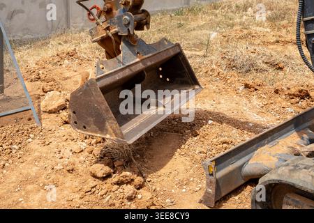 Nahaufnahme des Metallschaufels eines Baggers, der über gestörter Erde und trockener Vegetation steht und bereit für Aushubarbeiten ist Stockfoto