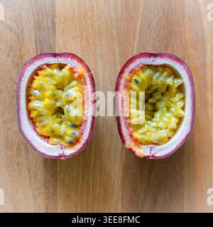 Zwei Hälften aus Passionsfrucht auf einem Schneidebrett aus Walnuss, auf dem Samen und Fruchtfleisch gezeigt werden. Gemeinsame Purpurfrucht (wissenschaftlicher Name: Passiflora edulis). UK Stockfoto
