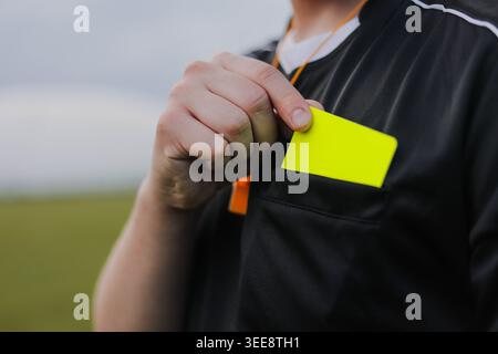 Der Fußballschiedsrichter nimmt eine gelbe Karte aus der Tasche auf dem Spielfeld und bereitet sich darauf vor, einen Spieler zu bestrafen. Konzept der Durchsetzung von Regeln und des Fairplay im Fußball. Stockfoto