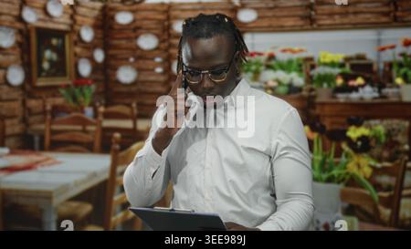 Der Mann hält das Telefon an das Ohr und liest die Zwischenablage im Inneren des Restaurantgebäudes, trägt ein weißes Hemd und eine Brille; Konzentration und Professionalität. Stockfoto