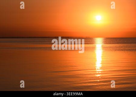 Sonnenuntergang über dem glatten Meer, goldener und orangener Himmel reflektiert auf dem Wasser, Horizont, ruhige und friedliche Landschaft, ruhige Natur, ruhige Meereslandschaft Stockfoto