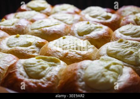 Ein Tablett mit frisch gebackenen, goldbraunen Vatrushka-Brötchen mit cremigen Käsefüllungen, ordentlich angeordnet und in einer Nahaufnahme unter warmem Licht glühend. Stockfoto