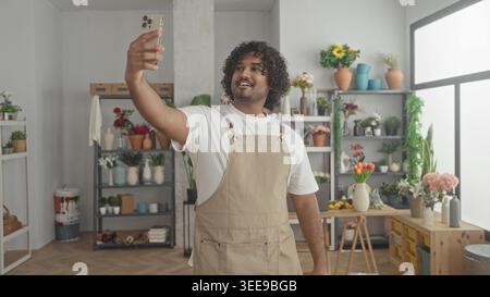 Mann Florist auf Schürze lächelnd, hält Smartphone und scrollend im Studio; zufriedene Unternehmerschaft Handwerk. Stockfoto