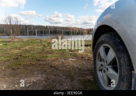 Autorad Von Lakeshore, Muddy Foreground, Der Kies Und Pfützen Umrahmt, Bedeckter Himmel Im Ruhigen Wasser, Distant Tree Line On Horizon, Quiet Roadside Stockfoto