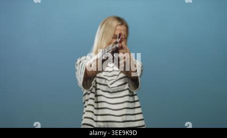 Blonde Frau mittleren Alters mit dunkler nasser Substanz an den Händen, die im Studio eine Fingerpistole zeigt; Verspieltheit Unfug. Stockfoto