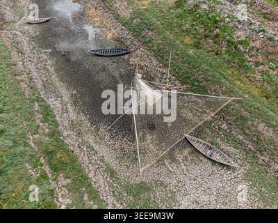 Aus der Vogelperspektive auf Holzboote und ein großes Fischernetz, das auf einem zerrissenen, ausgetrockneten Flussbett, umgeben von grünen Ufern in Natore, Rajshahi Division, B, gestrandet ist Stockfoto