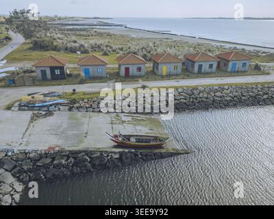 Blick aus der Vogelperspektive auf farbenfrohe Bunheiro-Strandhütten und Fischerboote an der ruhigen Küste, Bunheiro Port, Aveiro, Portugal. Stockfoto
