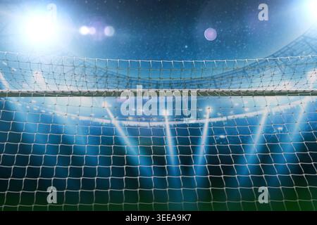 Blick durch ein Fußballnetz auf ein großes beleuchtetes Stadion bei Nacht mit hellen Flutlichtern, die eine dramatische, professionelle Sportatmosphäre schaffen Stockfoto