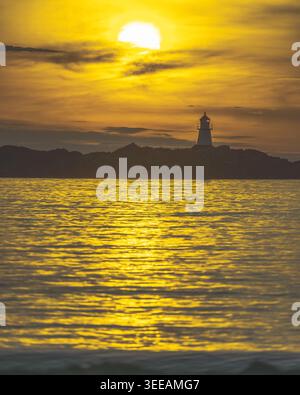 Dramatischer goldener Sonnenuntergang über ruhigem Meer mit Silhouetten des Leuchtturms Gimsoya auf einer kleinen Insel auf den Lofoten im Norden Norwegens, fotografiert im Sommer. A Stockfoto