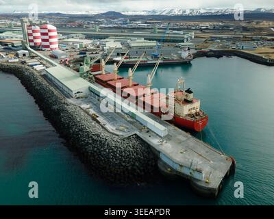 Hafnarfjordur, Island - 17. April 2026: Luftaufnahme des Industriehafens mit einem großen Frachtschiff, das neben einem Fördersystem angedockt und rot gestreift ist Stockfoto