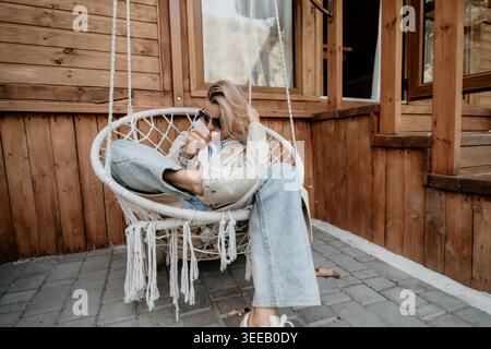 Frau, die sich in einem Hängestuhl auf einer hölzernen Veranda entspannt Stockfoto