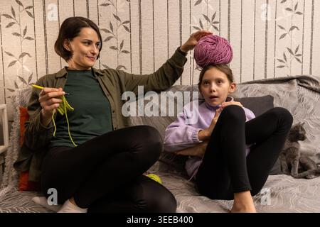 Mutter legt rosa Garnknäuel auf den Kopf der Tochter Stockfoto