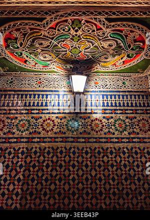 Verzierte Keramikfliesen und geschnitzte Decke beleuchtet durch eine Lampe im Snack Rcif Café Riad in der alten Medina, 08. August 2025, Fes, Marokko Stockfoto