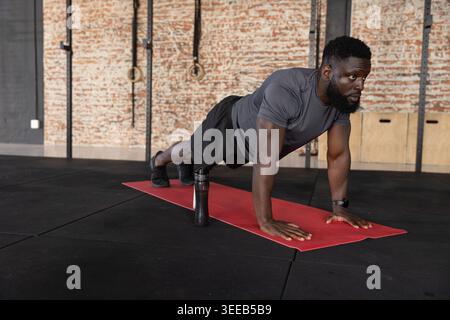 Auf roter Matte im Fitnessstudio, Afroamerikaner in grauem Hemd, Wasserflasche in der Nähe Stockfoto